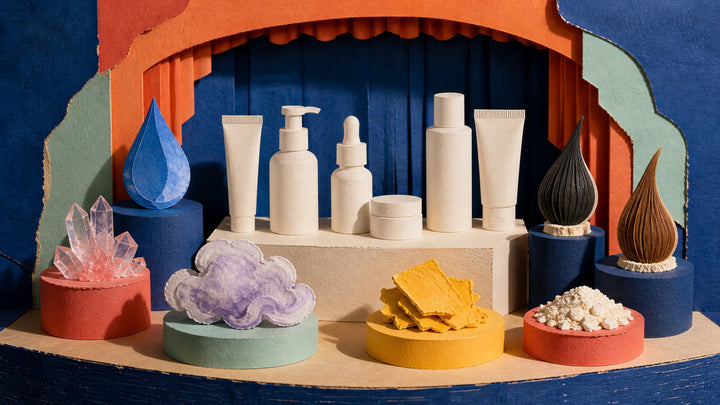 Eight abstract ingredient specimens surrounding six unbranded cosmetics in a colorful paper theatre